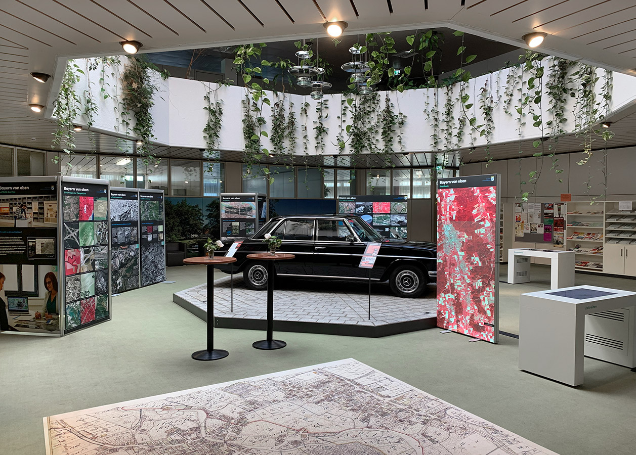Wanderausstellung "Bayern von oben" in Krumbach Blick in den Ausstellungsraum mit Touch-Bildschirmen sowie Ausstellungstafeln mit Bildern und Texten.