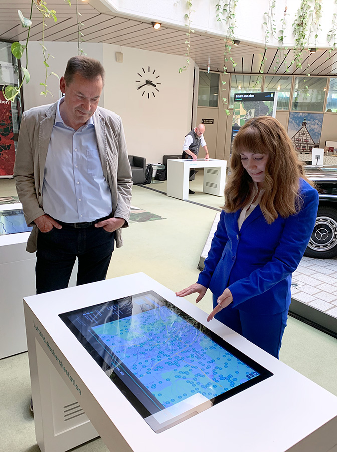 Wanderausstellung "Bayern von oben" in Krumbach Blick in den Ausstellungsraum, im Vordergrund Krumbachs Bürgermeister Hubert Fischer und Ann-Kathrin Johner, stellv. Leiterin Bayerisches Landesluftbildzentrum, an einem Touch-Bildschirm.