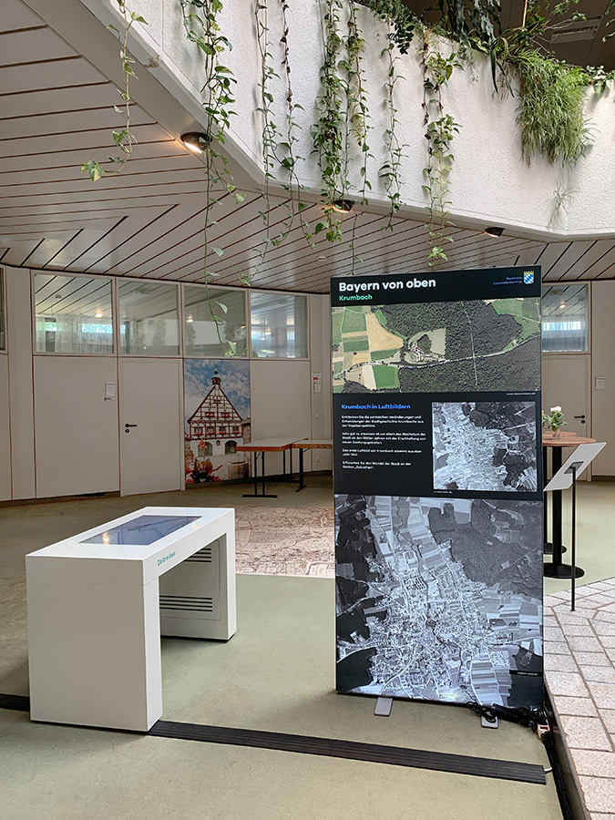 Wanderausstellung "Bayern von oben" in Krumbach Blick in den Ausstellungsraum, im Vordergrund eine Ausstellungstafel mit Luftbildern von Krumbach.